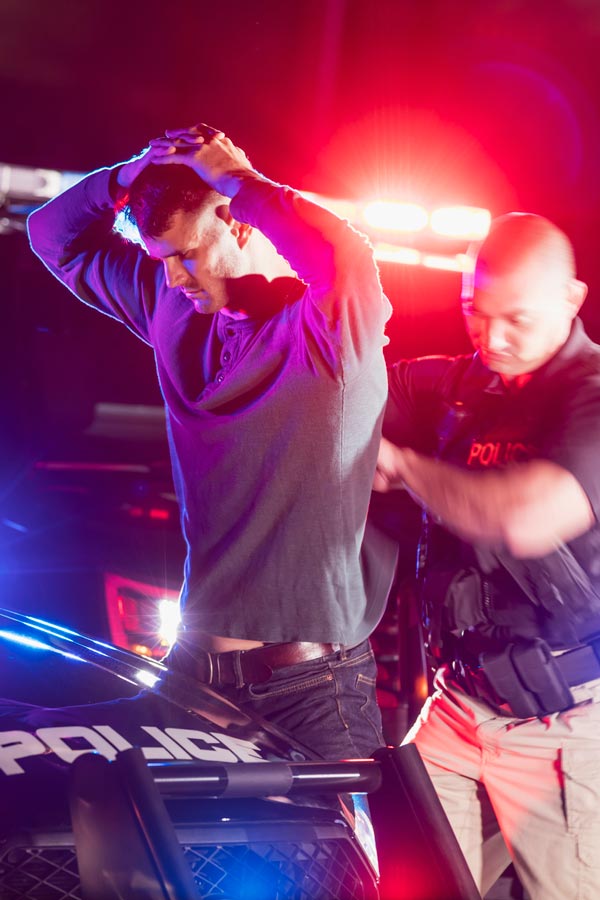 man with hands over head being arrested by police