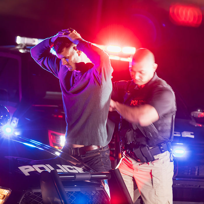 man with hands over head being arrested by police